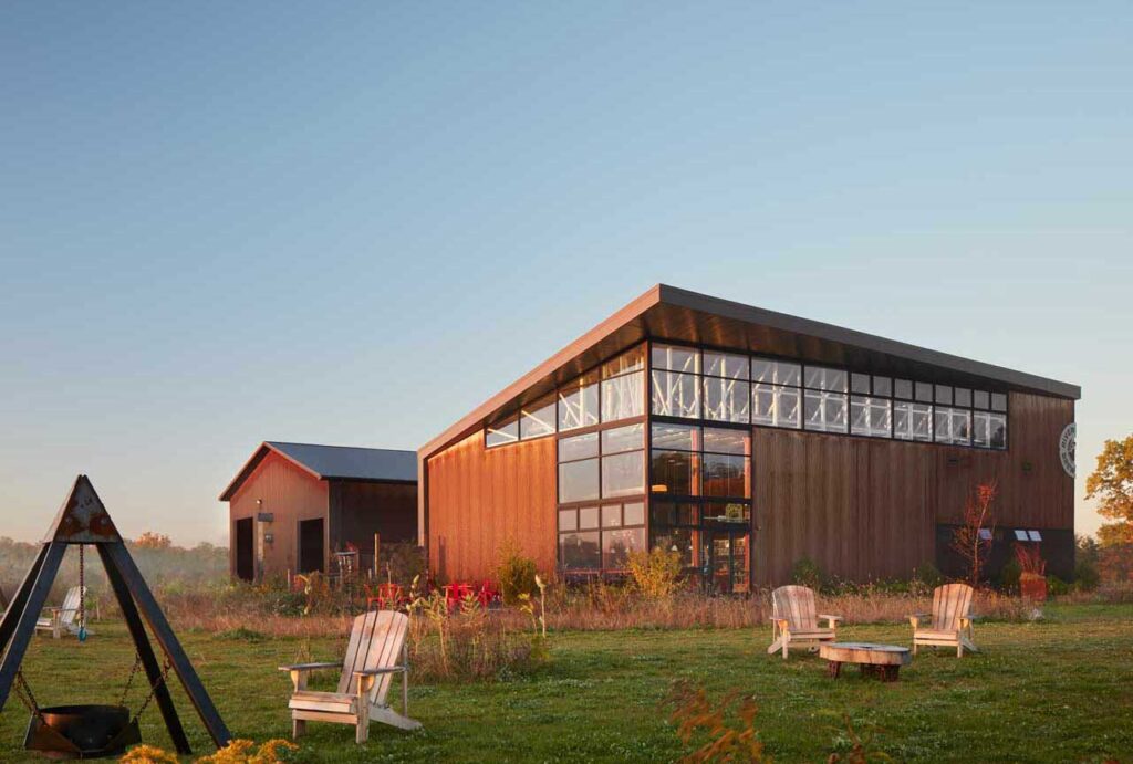 River St. Joe Brewery in Buchanan, Michigan, a dark wood-clad barn-style building with large windows set on a lawn with Adirondack chairs