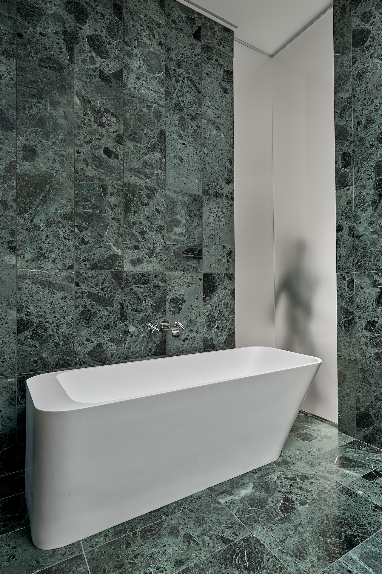green marble tile bathroom with soaking tub, skylights and frosted glass wall
