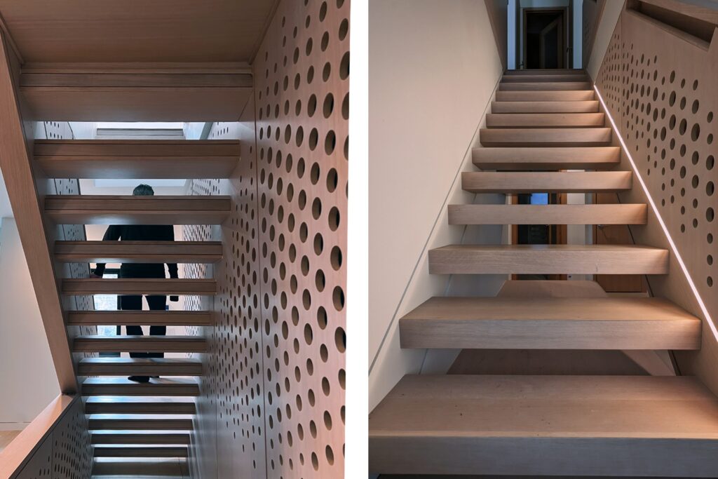 A person in dark clothing is seen from below, walking up a modern wooden staircase with open risers and perforated walls, illuminated by natural light from above, on the right is a similar staircase without a person walking.