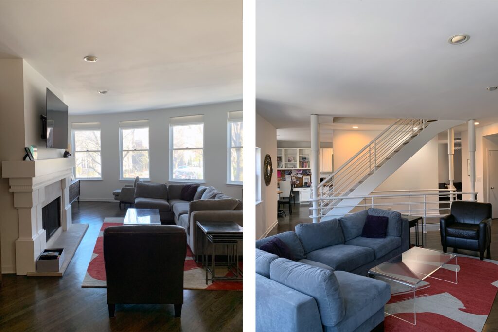 A modern living room featuring a fireplace, large windows, and two seating areas with sofas. On the right, a view of a staircase leading to a second floor with an open layout.