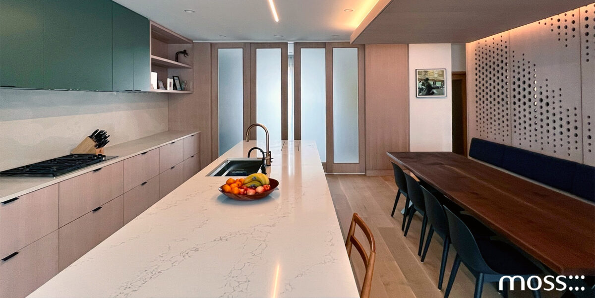 Modern Townhome Renovation with a modern kitchen and dining area with a marble island, fruit bowl, built-in sink, and stove. Wooden cabinets, frosted glass siding doors, and a long dark walnut dining table with black chairs are visible under warm, recessed lighting