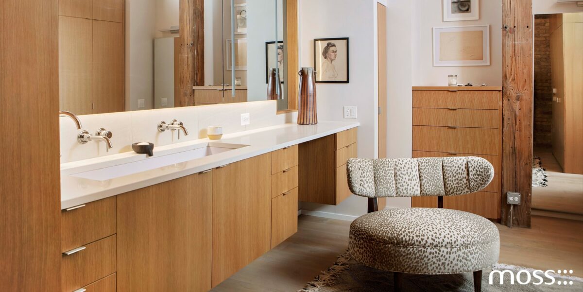 Custom home bathroom by Moss with warm wood vanity cabinetry, integrated sink, and a textured upholstered stool